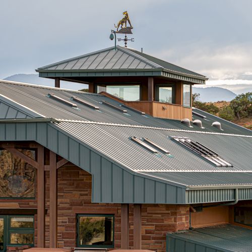 A building with a gray metal roof and multiple windows, featuring a small observation deck topped with a sculpture or weather vane.
