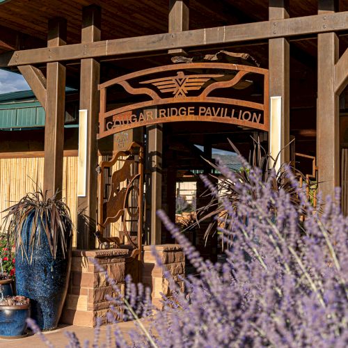 The image shows the entrance to the Lounge Bridge Pavilion, featuring wooden beams, potted plants, and decorative elements under a blue sky.