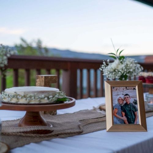 A decorated table with a cake, flowers, and a framed photo, set outdoors.