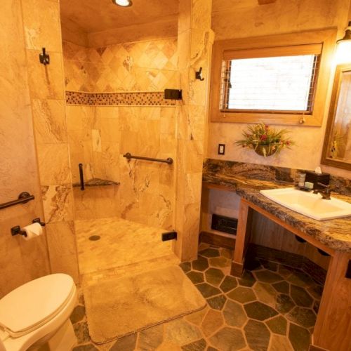 The image shows a bathroom with beige tiles, a shower area, toilet, sink with a mirror, and decorative lighting above the mirror.