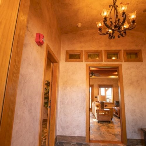 This image shows a warmly lit hallway with a chandelier, wooden doors, and a view into a cozy living room at the end.