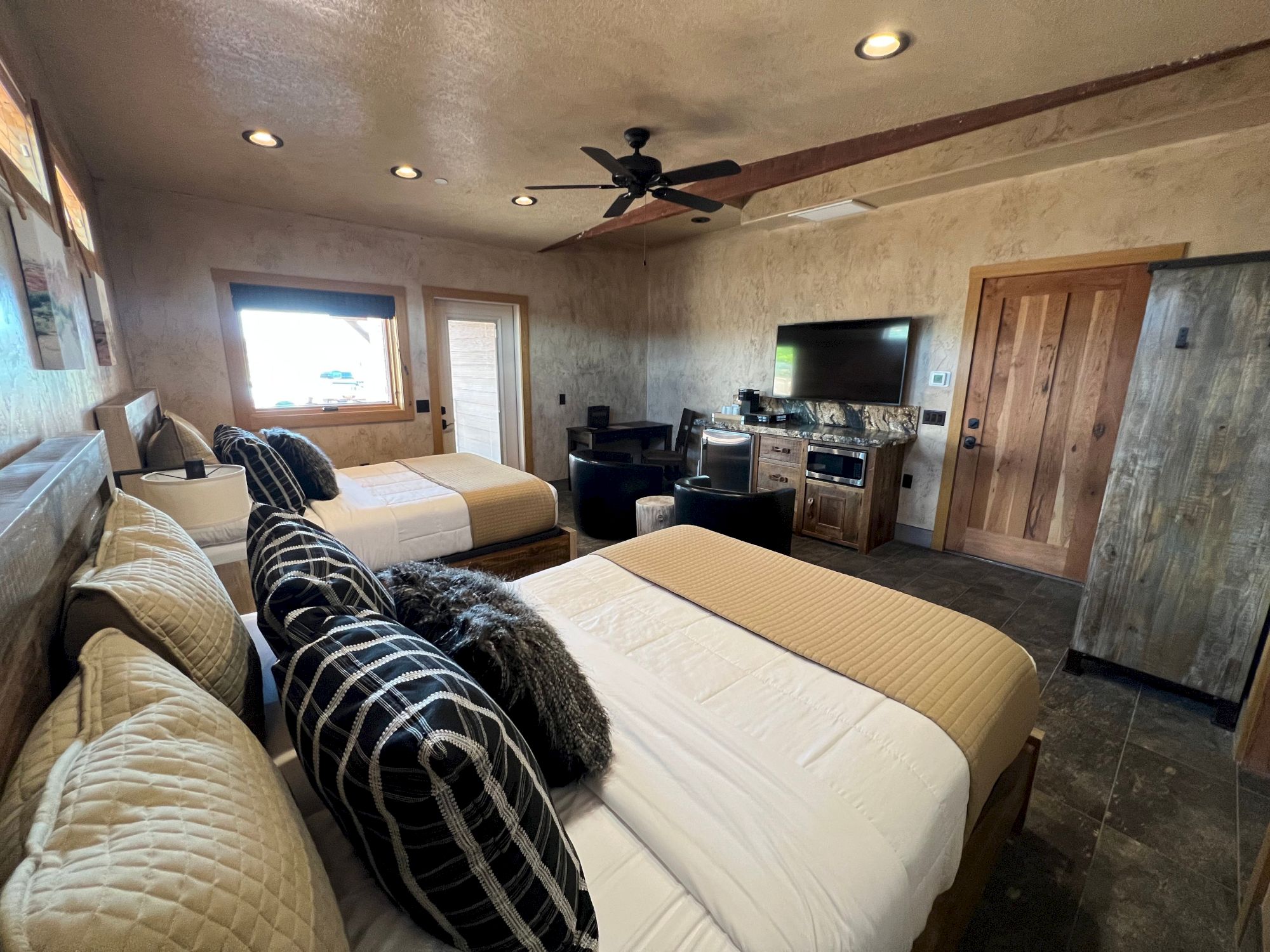 A cozy bedroom with two beds, patterned pillows, a TV, mini-fridge, and wooden decor, exuding a rustic and comfortable vibe.