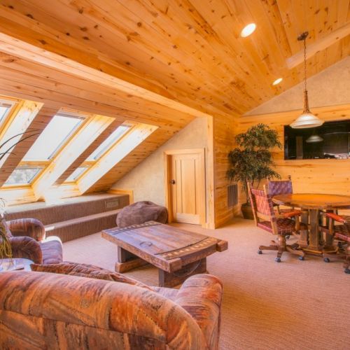 A cozy wooden attic room with skylights, chairs, a table, and a flat-screen TV.