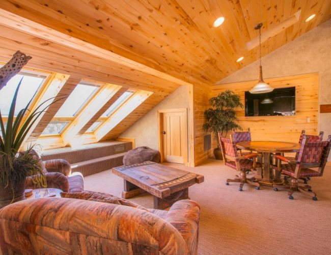 A cozy wooden attic room with skylights, chairs, a table, and a flat-screen TV.