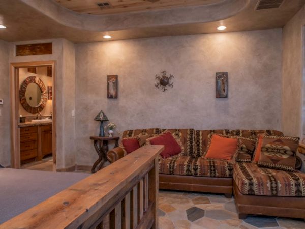 A cozy room features a rustic couch with patterned cushions, wooden accents, decorative wall art, and a glimpse into a bathroom.