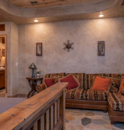 A cozy room features a patterned sofa, wooden accents, decorative pillows, wall art, and a view into a bathroom with a round mirror.