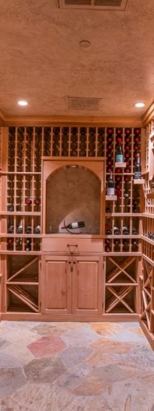 A wine cellar with wooden shelves, bottles lined up, and a central cabinet against the back wall.