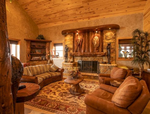 A cozy living room with a rustic vibe, featuring a stone fireplace, wooden ceiling, sofas, armchairs, and decorative plants for warmth.