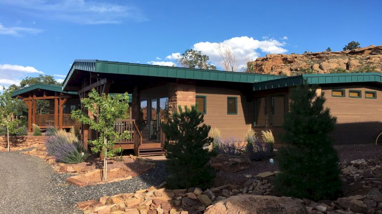 A modern, single-story building with a green roof, surrounded by rocks and trees under a clear blue sky.