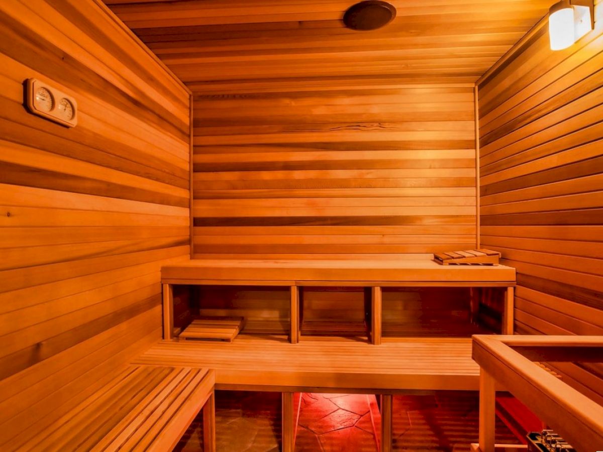 The image shows a wooden sauna interior with benches, a light fixture, and warm lighting creating a cozy atmosphere.